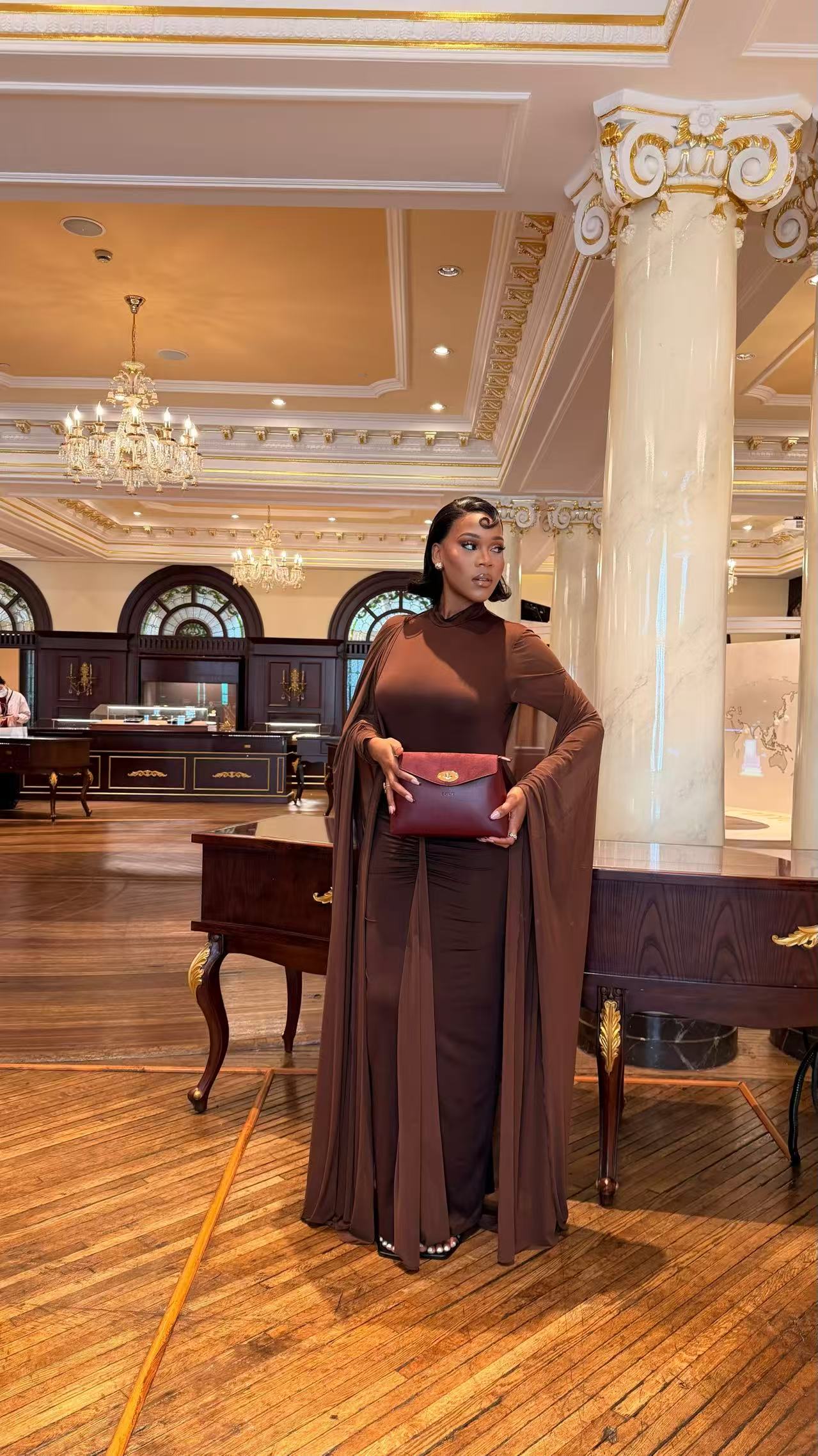 Model in a brown outfit carrying the burgundy Adaline bag in an ornate interior